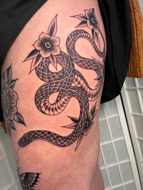 A black and grey tattoo of a snake intertwined with flowers on the thigh, featuring bold lines and traditional styling — by Megan Rose, los angeles