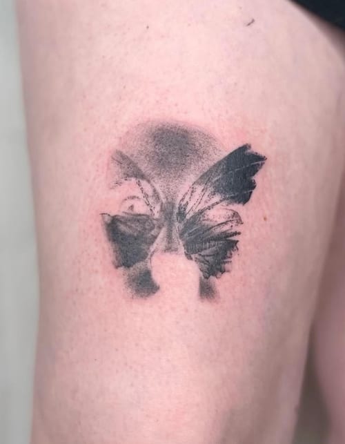 An abstract black and grey tattoo on the thigh, depicting a fragmented face with butterfly wings — by Level tattoo, los angeles