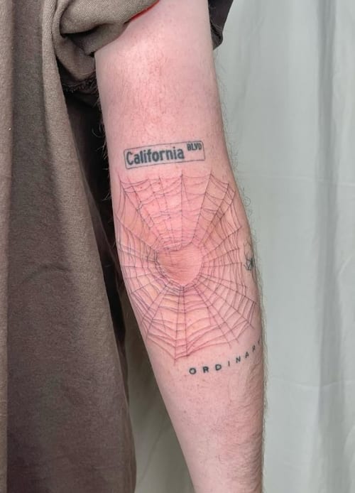 A minimalist black and grey linework tattoo of a spider web on the forearm, with simple lines and subtle shading — by Level tattoo, los angeles