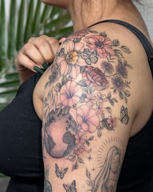 A delicate floral bouquet with butterflies and an earth motif on the shoulder, featuring a mix of color and black ink — by Melanie Benoit, los angeles