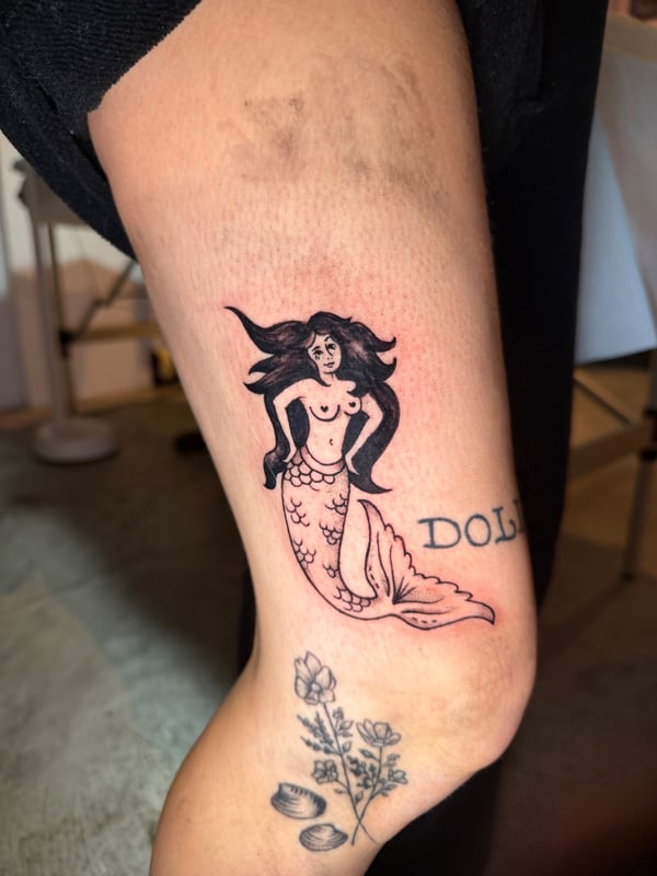 A bold black and grey traditional mermaid tattoo on the leg, featuring classic mythological elements — by Kiera Garvin, los angeles