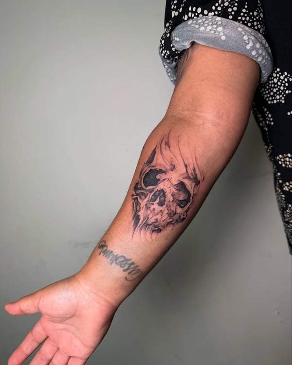 A bold black and grey skull tattoo on the forearm with realistic shading and dark tones — by zealous, los angeles