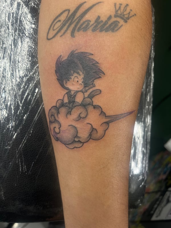 A colorful anime-style tattoo of Goku riding a cloud on the forearm, accompanied by script lettering above — by Mr._Folks, los angeles