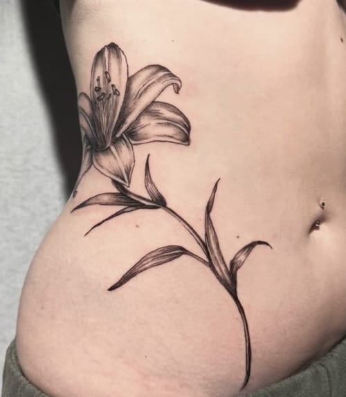A fine line black and grey tattoo of a lily flower on the rib, featuring delicate linework and shading — by Shelby Bianco, los angeles