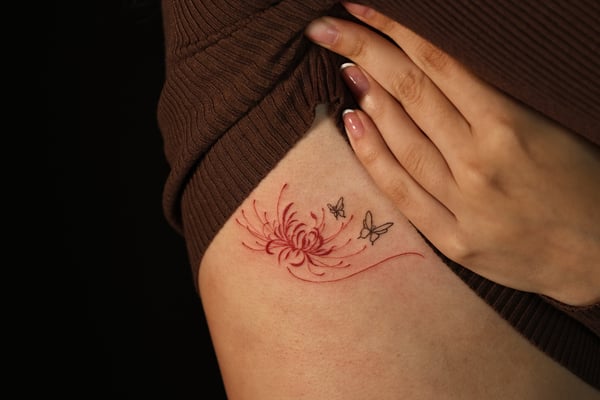 A minimalist fine line tattoo on the hip featuring a red flower with delicate butterflies, using subtle color accents — by gloria.shi.ink, alhambra, ca