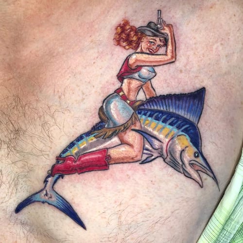 A colorful and whimsical tattoo of a cowgirl riding a fish on the chest, done in a bold New School style — by Sandra Price, los angeles