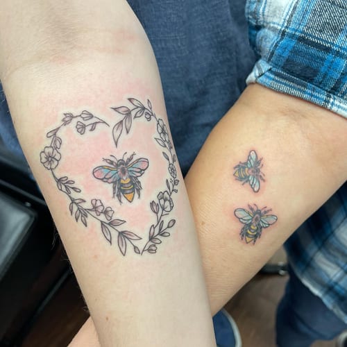 A delicate bee tattoo with a floral heart design on the forearm, featuring fine line work and subtle colors — by Sandra Price, los angeles