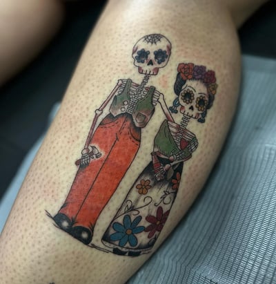 A colorful skeleton couple tattoo on the leg with floral details — by Maddie Ramirez, los angeles