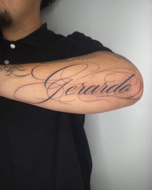 A black and grey script tattoo on the forearm featuring elegant cursive lettering — by ashynucklestattoo, los angeles