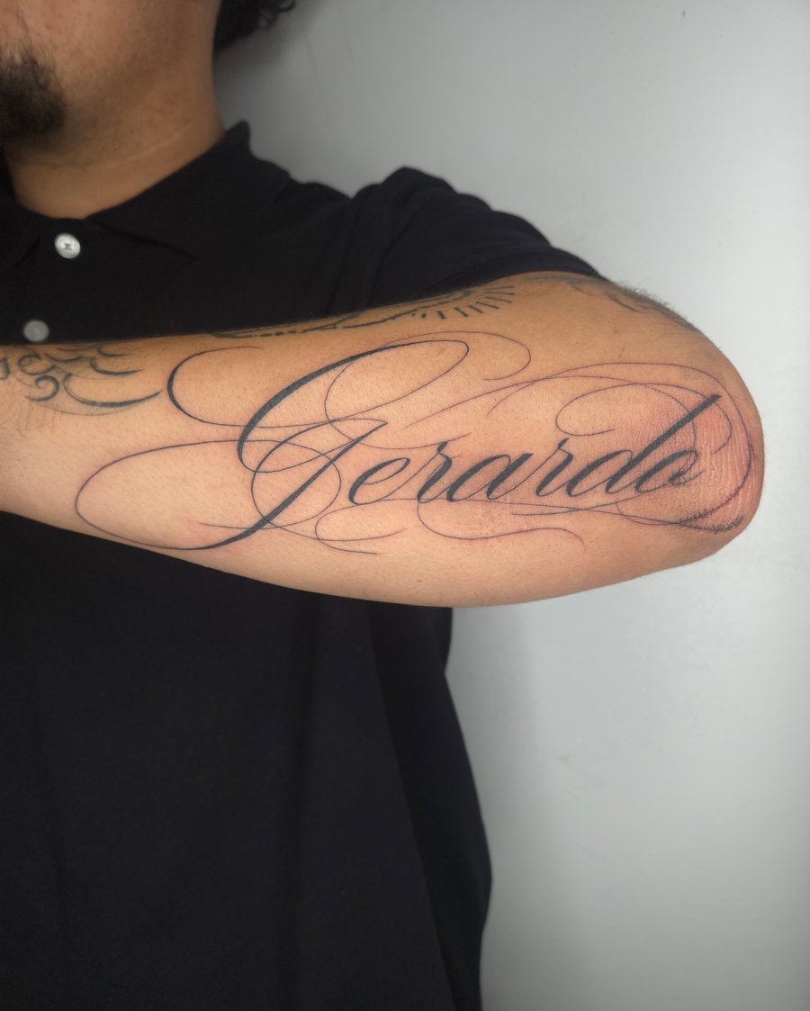 A black and grey script tattoo on the forearm featuring elegant cursive lettering — by ashynucklestattoo, los angeles