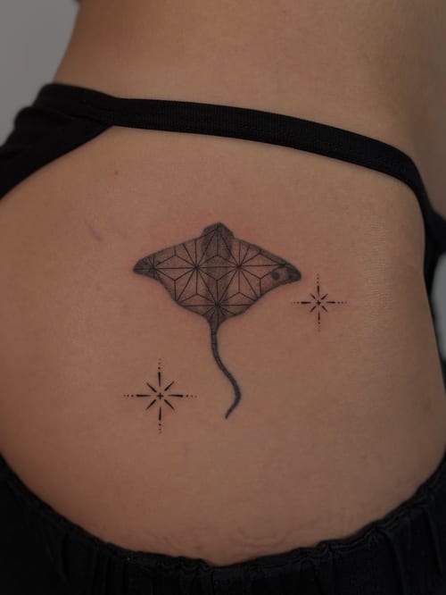 A black and grey geometric manta ray tattoo on the hip, featuring intricate line patterns and star-like accents — by Rae kaku, los angeles