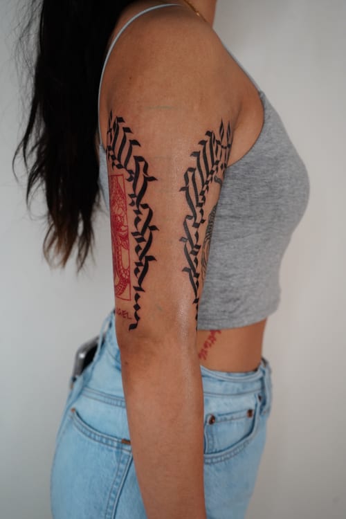 sharp calligraphic blackwork strips running down the front and back of the upper arm — by brian kies, los angeles
