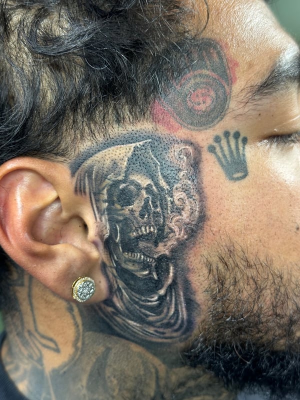 A black and grey skull tattoo on the face, featuring dotwork shading and bold outlines — by Humilde tattoos, los angeles