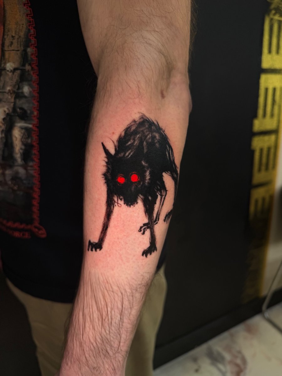 A dark blackwork tattoo of a creepy creature with red eyes on the forearm, featuring a graphic and eerie style — by Kiera Garvin, los angeles