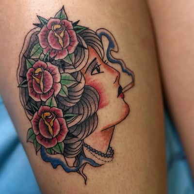 A bold neo-traditional tattoo of a woman's portrait with roses and a cigarette, featuring vibrant colors and blackwork shading — by Maddie Ramirez, los angeles