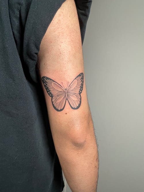 A delicate black and grey butterfly tattoo on the upper arm with fine line details — by Brian Kies, los angeles