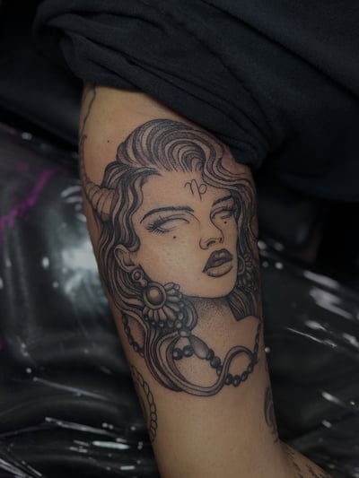A bold blackwork tattoo of a woman's portrait with a Capricorn symbol on the upper arm — by Maddie Ramirez, los angeles