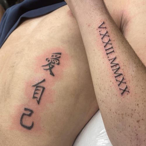 A minimalist black and grey tattoo featuring Chinese characters and Roman numerals on the arm — by Sandra Price, los angeles
