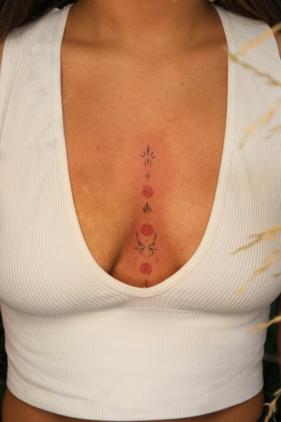 A minimalist tattoo on the sternum featuring celestial symbols in a vertical arrangement with subtle color accents — by gloria.shi.ink, los angeles