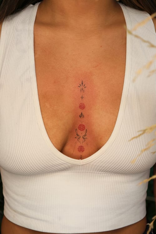 A minimalist tattoo on the sternum featuring celestial symbols in a vertical arrangement with subtle color accents — by gloria.shi.ink, los angeles