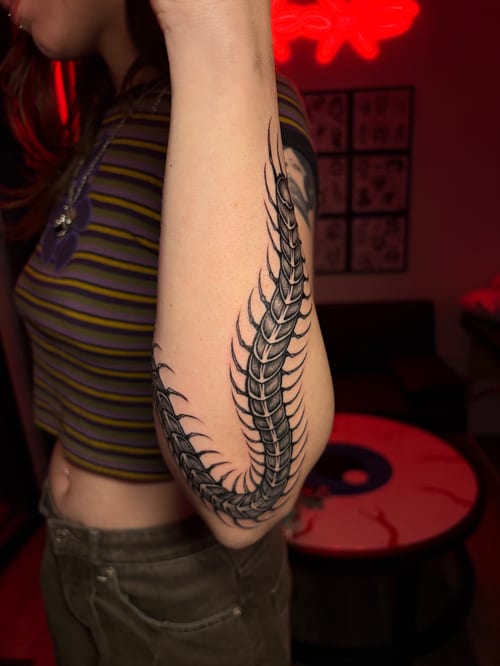 large blackwork centipede curving around the elbow from upper arm to forearm — by vince espinoza, los angeles