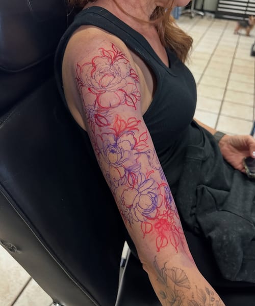 A delicate floral design tattoo on the upper arm featuring linework flowers in color — by Melanie Benoit, los angeles