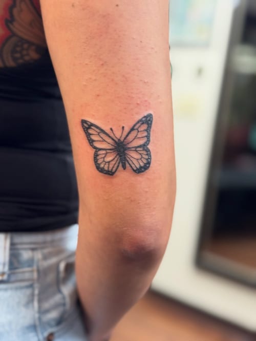 A delicate black and grey butterfly tattoo on the arm in a minimalist style — by Sandra Price, los angeles