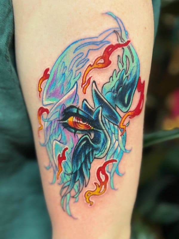 A vibrant neo-traditional tattoo of a stylized bird with flames on the upper arm, featuring bold colors and dynamic lines — by Tweetwee, west covina, ca