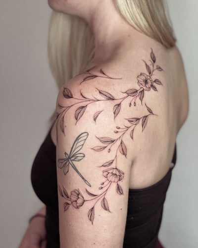A delicate black and grey tattoo of a dragonfly and floral vine on the shoulder, featuring fine line work and minimalistic design — by Melanie Benoit, los angeles