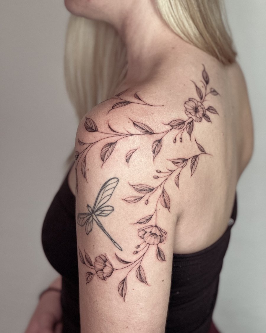 A delicate black and grey tattoo of a dragonfly and floral vine on the shoulder, featuring fine line work and minimalistic design — by Melanie Benoit, los angeles