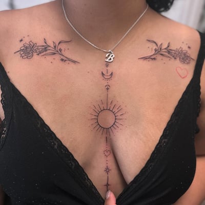 A fine line black and grey tattoo on the chest featuring birth flowers and celestial elements like the sun and moon — by Maddie Ramirez, los angeles