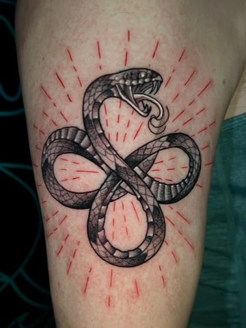 A Neo-Traditional snake tattoo on the upper arm, featuring black and grey scales with red accent lines radiating outward — by Josue Bravo, los angeles