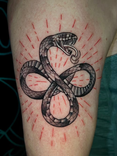 A Neo-Traditional snake tattoo on the upper arm, featuring black and grey scales with red accent lines radiating outward — by Josue Bravo, los angeles