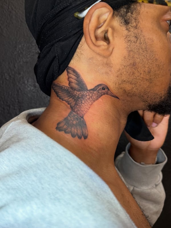 A realistic black and grey hummingbird tattoo on the neck, showcasing delicate details and shading — by Kiera Garvin, los angeles