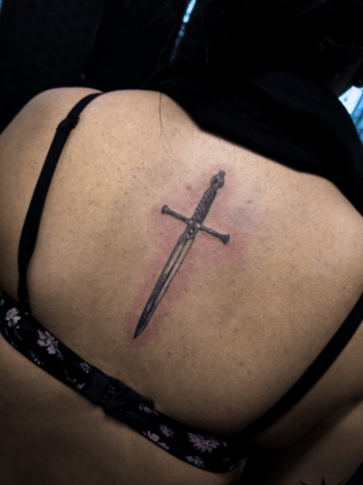 A minimalist black and grey sword tattoo on the back with clean lines and simple design — by Garrick {Gman} lee, los angeles