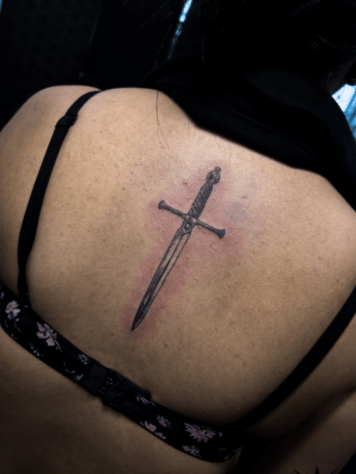 A minimalist black and grey sword tattoo on the back with clean lines and simple design — by Garrick {Gman} lee, los angeles