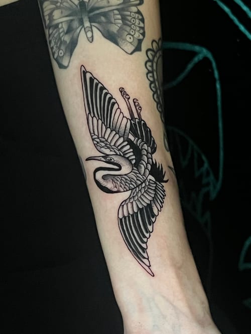 A black and grey linework tattoo of a bird in flight on the forearm, featuring bold outlines and detailed feather patterns — by Josue Bravo, los angeles