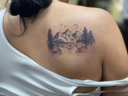 A delicate black and grey mountain landscape tattoo on the back, featuring trees and a crescent moon in a fine line style — by Sandra Price, los angeles