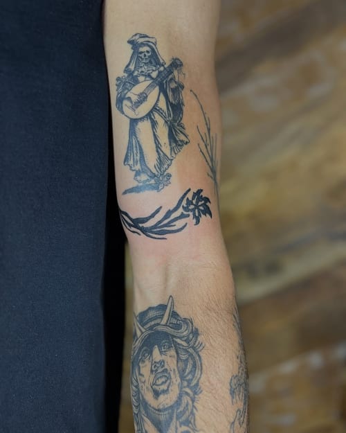 A black and grey tattoo of a skeleton playing a guitar on the forearm, done in a graphic blackwork style — by Dylan Aiello, los angeles