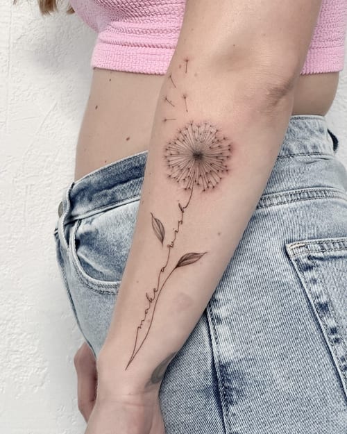 A delicate black and grey fine line dandelion tattoo on the forearm, featuring a minimalist design with floating seeds — by Melanie Benoit, los angeles