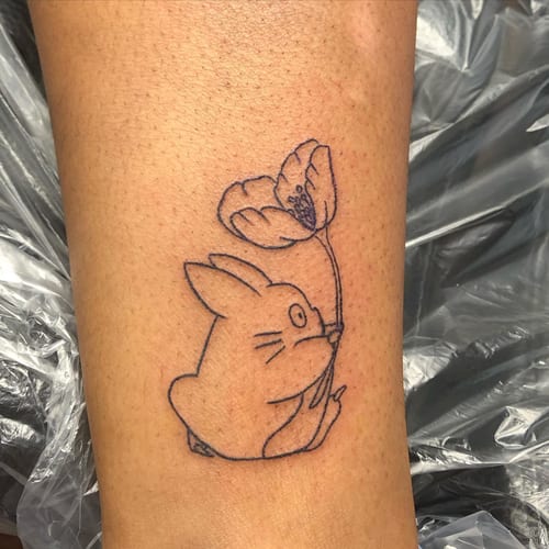 A minimalist linework tattoo of a cartoon rabbit holding a flower on the leg — by Sandra Price, los angeles