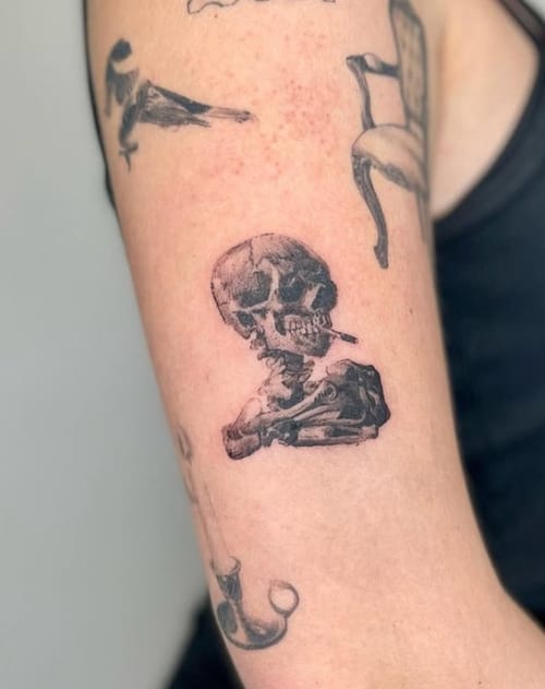 A black and grey sketch-style tattoo of a skull on the upper arm, featuring detailed line work and shading — by Level tattoo, los angeles