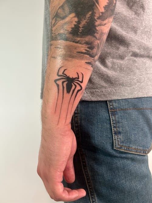 A black and grey linework tattoo of a stylized spider on the forearm, featuring bold lines and a minimalist design — by Brian Kies, los angeles