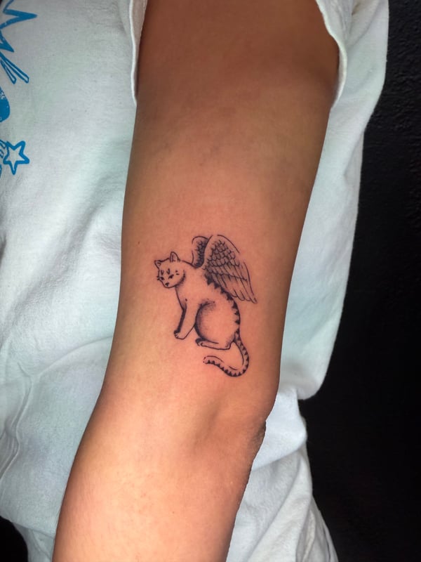 A minimalist black and grey tattoo of a winged cat on the forearm, featuring delicate linework — by Kiera Garvin, los angeles