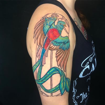 A vibrant and colorful bird tattoo on the upper arm, done in a neo-traditional style with bold outlines and ornate details — by Sandra Price, los angeles