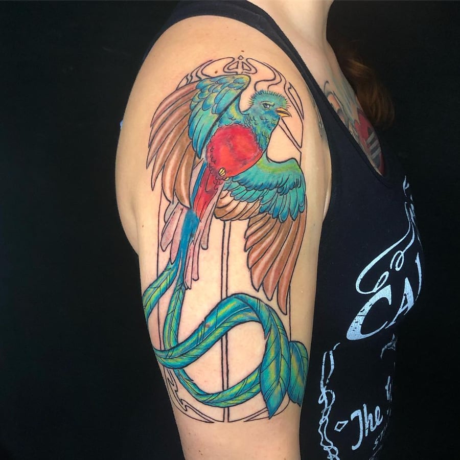 A vibrant and colorful bird tattoo on the upper arm, done in a neo-traditional style with bold outlines and ornate details — by Sandra Price, los angeles