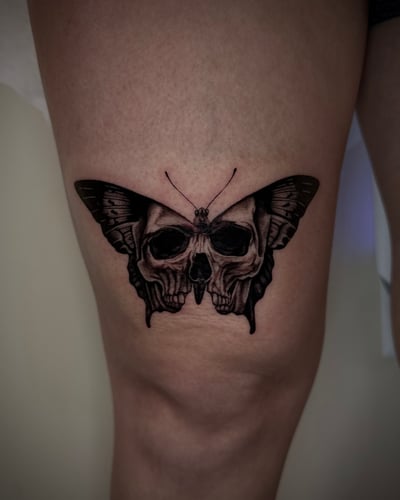 A black and grey surrealistic tattoo of a butterfly with skulls integrated into its wings on the thigh — by emily, los angeles