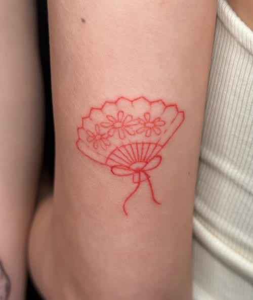 A minimalist red linework tattoo of a fan with floral patterns on the arm — by Samantha Wilks, los angeles