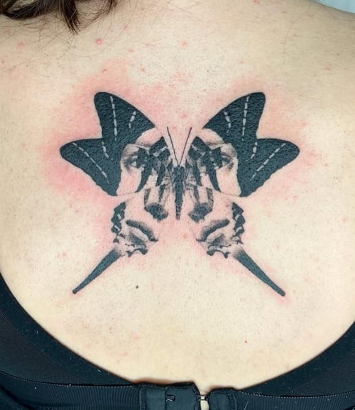 A black and grey abstract butterfly tattoo on the back, incorporating facial elements within the wings — by Level tattoo, los angeles