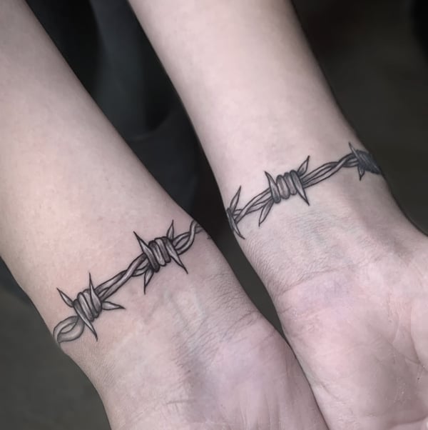 A minimalist black and grey barbed wire tattoo encircling the wrist with clean lines and simple design — by Shelby Bianco, ventura, ca